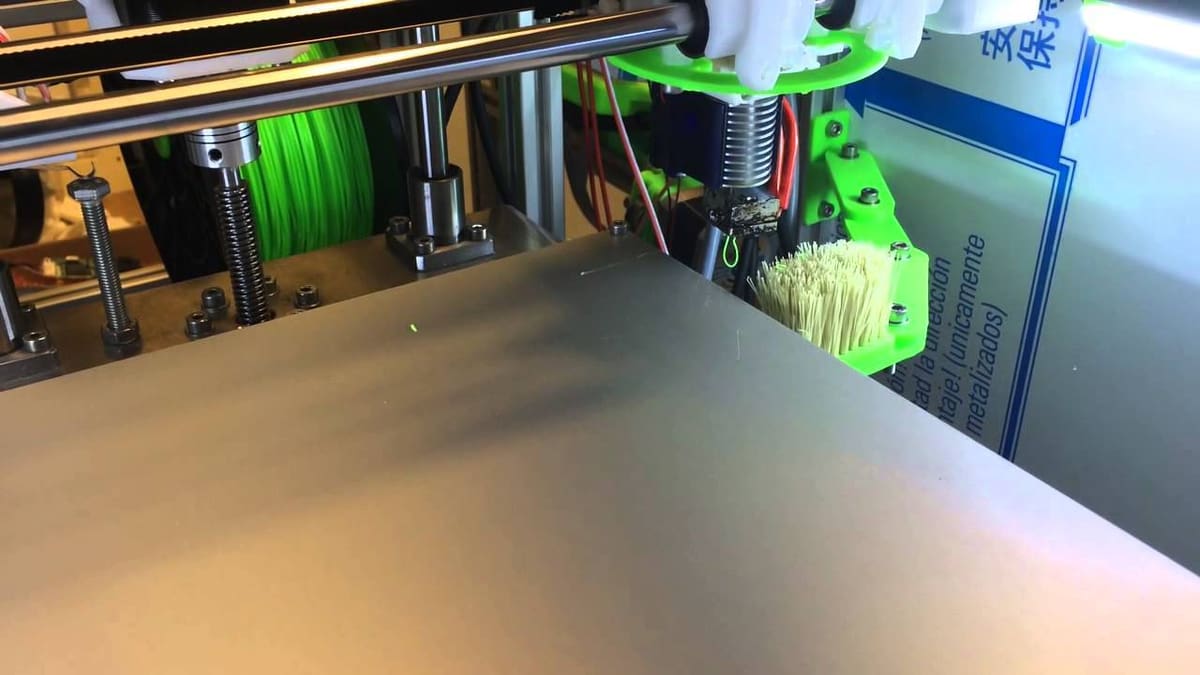 Brush mounted on the side of the bed. G-code can be used to make the hot end wipe off any residue prior to printing.